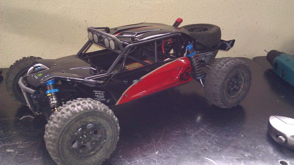 Black and red RC buggy with roll cage, spare tire on back, and off-road tires