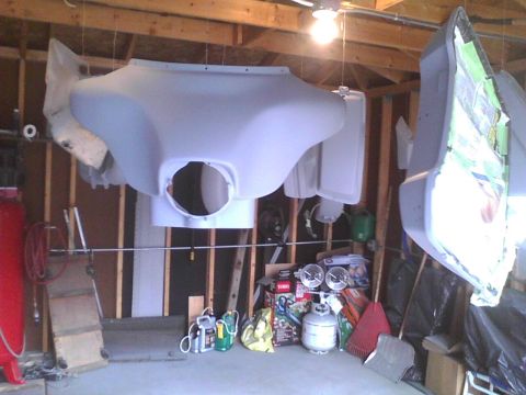 2003 Ford Crown Victoria - Two large motorcycle fairings are suspended in a garage, awaiting further work.