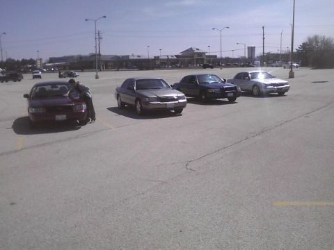 2003 Ford Crown Victoria - A group of sedans, including a maroon 2003 Ford Crown Victoria, are parked in an outdoor lot.