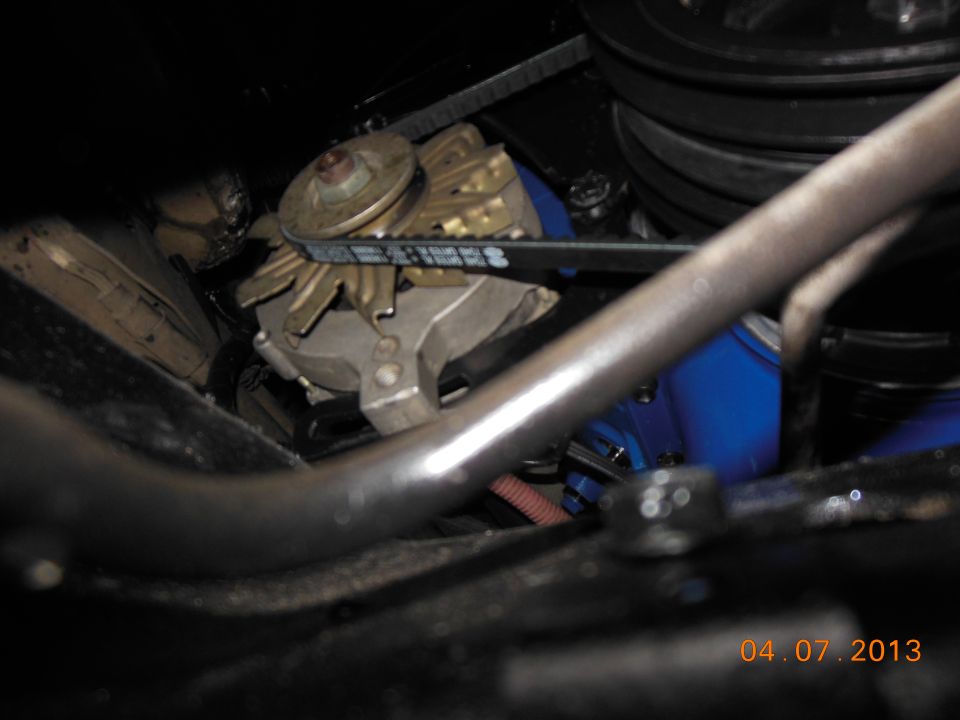 Close-up of an alternator with a V-belt routed around its pulley. Blue painted engine component visible behind