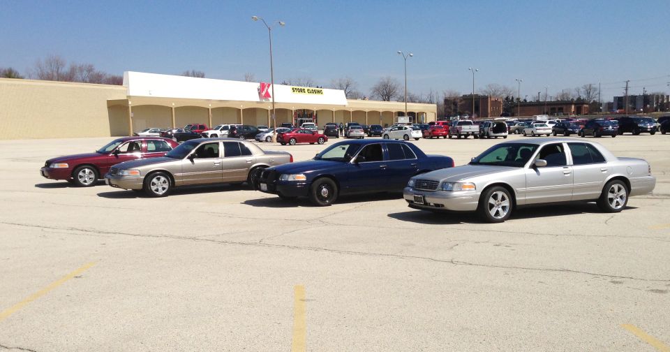 Four Ford Crown Victorias parked in a lot, including two police-style cars