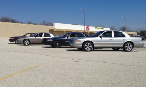 2005 Ford Crown Victoria - Several Ford Crown Victorias are parked in a lot in front of a store.