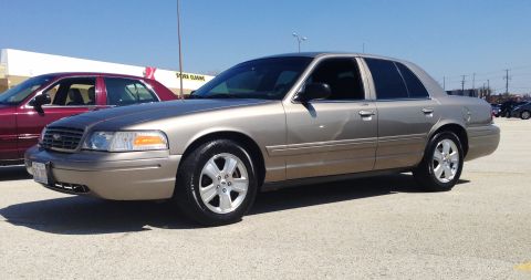 2005 Ford Crown Victoria - Two Ford Crown Victorias parked outside a store on a sunny day.