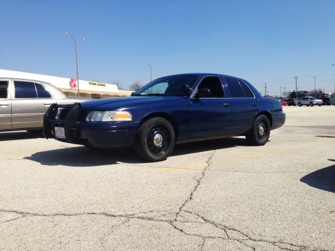 2005 Ford Crown Victoria - A dark blue sedan, possibly a police car, is parked in a lot under a clear sky.