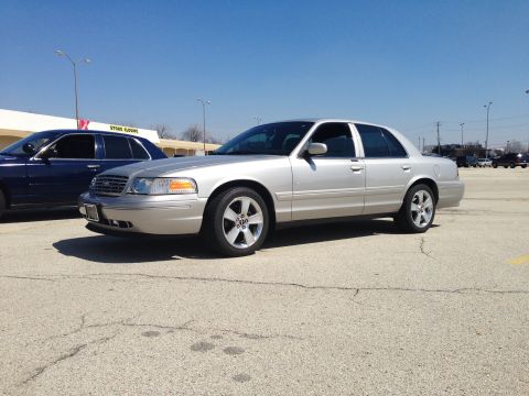 2005 Ford Crown Victoria - A silver sedan is parked in a lot next to a blue sedan under a clear sky.