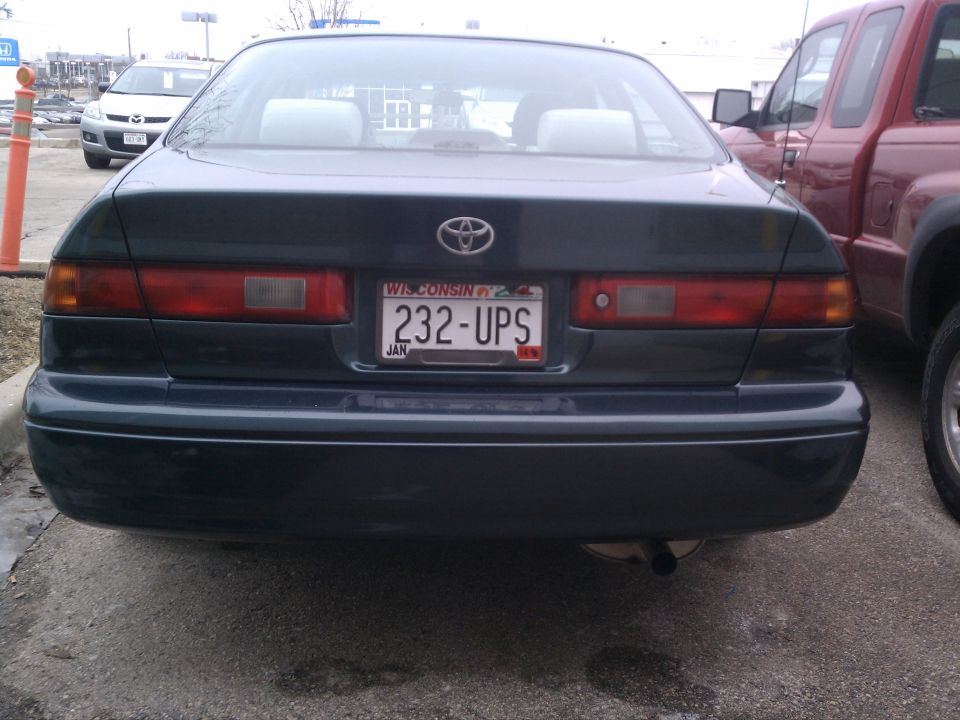 Rear of a dark 1998 Toyota Camry with Wisconsin plates 232-UPS. Red pickup truck is parked to the right