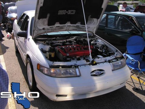 1993 Ford Taurus - A white Ford Taurus SHO is displayed with its hood open, revealing its engine bay and red intake manifold.