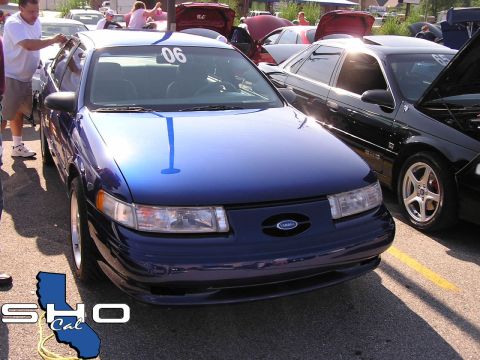 1993 Ford Taurus - A blue Ford Taurus is parked next to a black car, both with hoods open at an outdoor car show.