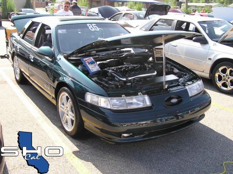 1993 Ford Taurus - Green Ford Taurus at a car show, hood open revealing the engine. Another vehicle is visible to the right.