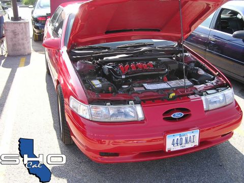 1993 Ford Taurus - A red 1993 Ford Taurus is shown from the front with its hood open, revealing the V6 engine. Another car is visible in the background.