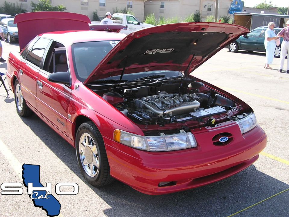 Red 1996 Ford Taurus SHO sedan, front 3/4 view, hood open revealing engine, chrome wheels, slight damage on front bumper