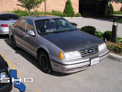 1993 Ford Taurus - A silver Ford Taurus with a matte black hood is parked in a lot. The car has a number 55 on its windshield.
