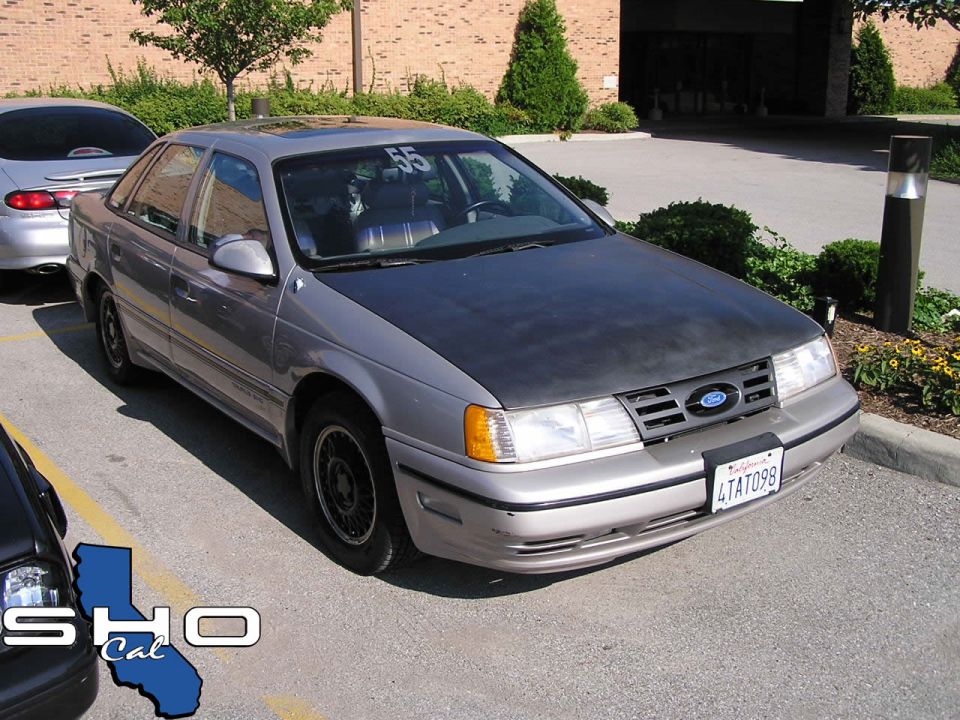 Silver Ford Taurus with a matte black hood, parked next to another car. Number 55 is on the windshield