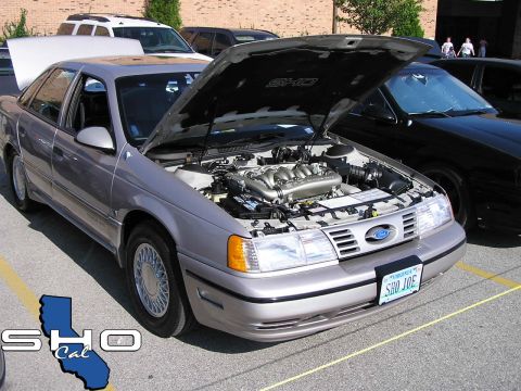 1993 Ford Taurus - A silver 1993 Ford Taurus is displayed with its hood open, the engine. The vehicle is parked outdoors with other cars visible.