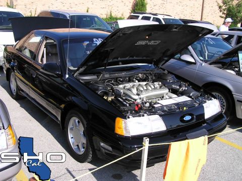 1993 Ford Taurus - A black Ford Taurus SHO is displayed with its hood open, revealing the engine, at an outdoor car event.
