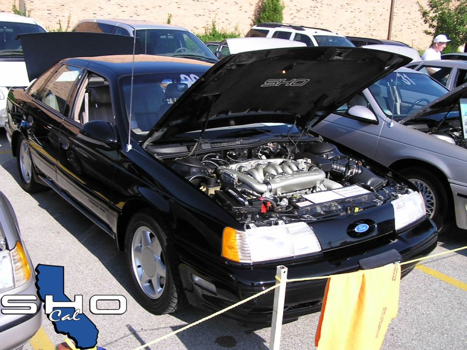 Black Ford Taurus SHO with hood open showing engine. Another Taurus is parked next to it