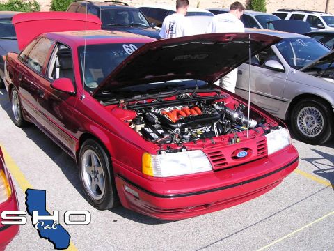 1993 Ford Taurus - A red 1993 Ford Taurus is displayed with its hood open, revealing the engine bay at a car show.