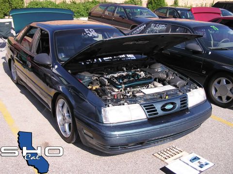 1993 Ford Taurus - A dark blue 1993 Ford Taurus is displayed with its hood open, revealing the engine, at a car show.