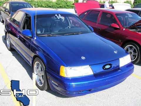 1993 Ford Taurus - A blue 1993 Ford Taurus is parked next to a red car, with racing seats visible inside.