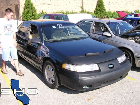 1993 Ford Taurus - A black Ford Taurus is parked at an outdoor event, with a car cover obscuring its front end.
