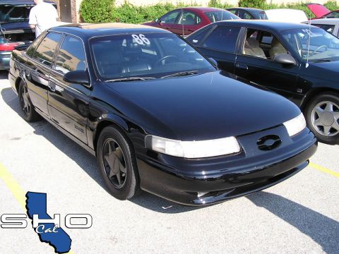 1993 Ford Taurus - A black sedan is parked in a lot with other vehicles, displaying a competition number on its windshield.
