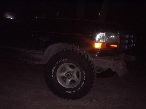 1993 Ford Bronco - A dark-colored Ford Bronco is partially visible at night, showing its front wheel and headlight assembly.