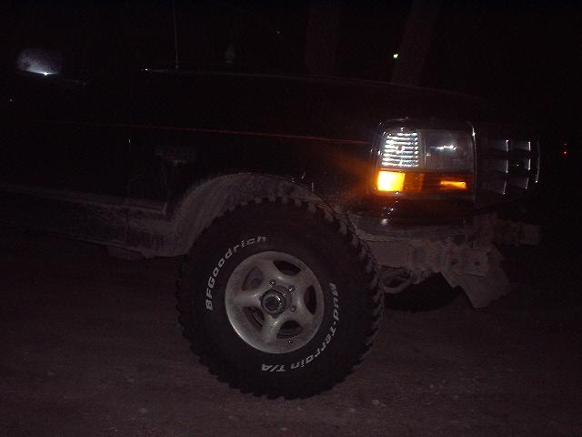 Black Ford Bronco front fender and tire, with headlight on. The vehicle appears to be from the early 1990s