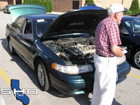 1993 Ford Taurus - A man examines the engine of a dark green Ford Taurus SHO, which has its hood open.