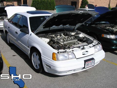 1993 Ford Taurus - A white Ford Taurus is parked with its hood open, revealing the engine, alongside other vehicles.