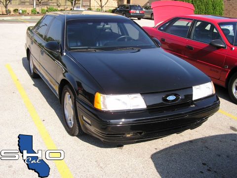 1993 Ford Taurus - A black Ford Taurus is parked in a lot next to a red car, with its front end facing the camera.