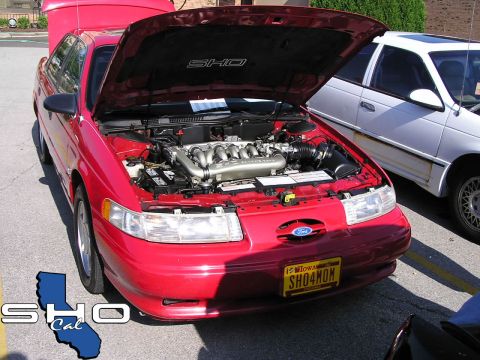 1993 Ford Taurus - A red 1992 Ford Taurus SHO is parked with its hood open, revealing the V8 engine, next to a white car.