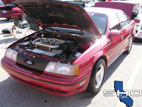 1993 Ford Taurus - A red Ford Taurus SHO sedan is parked with its hood open, displaying the engine bay.