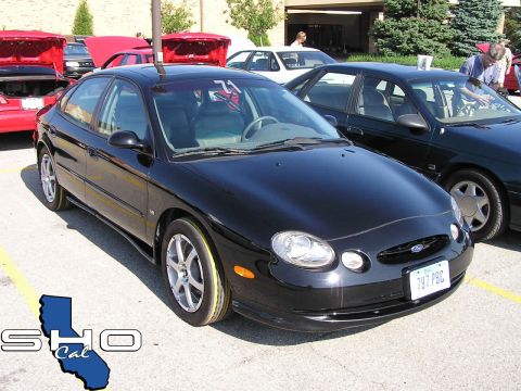 1993 Ford Taurus - A black Ford Taurus is parked at an outdoor car show, with other vehicles visible in the background.