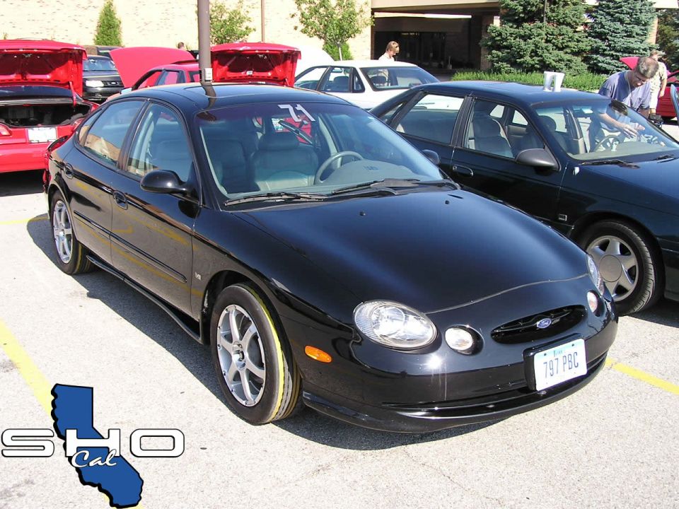Black Ford Taurus with yellow tire markings, parked at an outdoor event