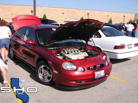 1993 Ford Taurus - A red sedan, likely a 1999 Ford Taurus, is displayed with its hood open, revealing a V8 engine. The license plate reads SOWHAT 9.