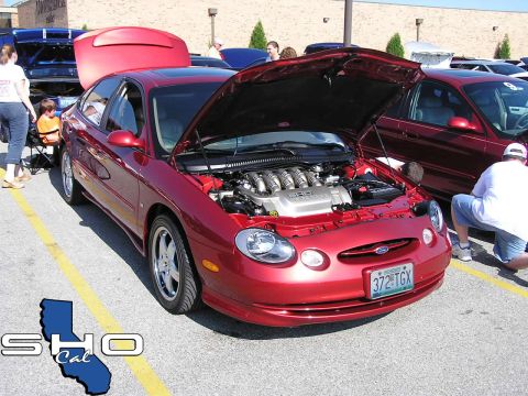 1993 Ford Taurus - Red Ford Taurus at a car show, hood open to reveal the engine. Other vehicles and people are visible.