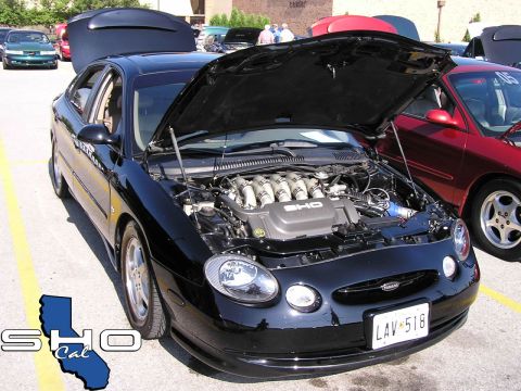 1993 Ford Taurus - Black Ford Taurus SHO at an event, hood open to display the V8 engine. Other vehicles are visible.