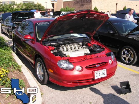1993 Ford Taurus - A red 1996 Ford Taurus is displayed with its hood open, revealing the engine, at an outdoor car event.