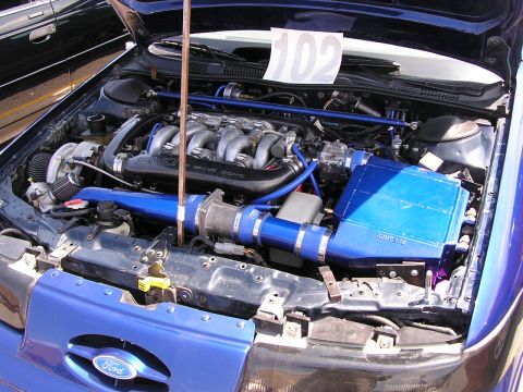 1993 Ford Taurus - The engine bay of a blue Ford Taurus features a modified V6 engine with a turbocharger and custom blue intake piping.