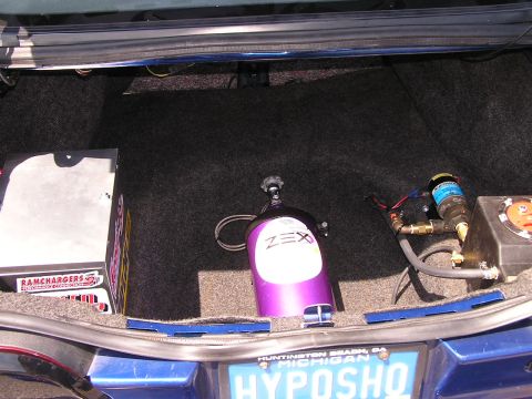 1993 Ford Taurus - The trunk of a blue vehicle contains a purple ZEX nitrous oxide bottle and a Ramchargers box, along with other performance parts.