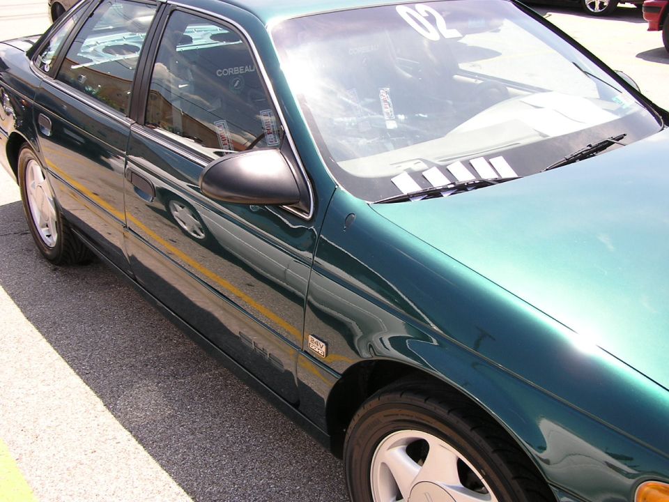 Green 1993 Ford Taurus sedan parked on asphalt, side view showing door, mirror, and wheel