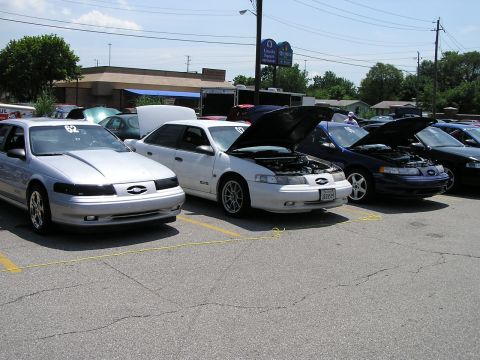 1993 Ford Taurus - Several Ford Taurus sedans are parked in a lot, with two having their hoods open.