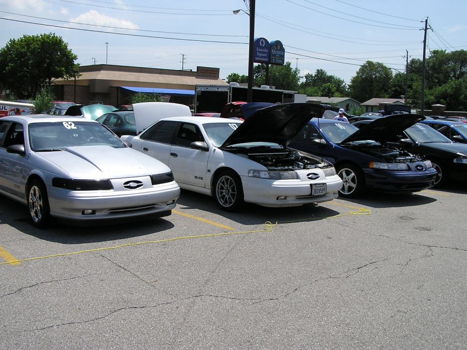 Three Ford Taurus sedans parked in a lot, hoods up on two of them. The front car has number 62 on its windshield