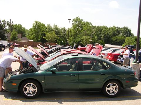 1993 Ford Taurus - A green sedan is parked with its sunroof open, while other vehicles in the background have their hoods raised.
