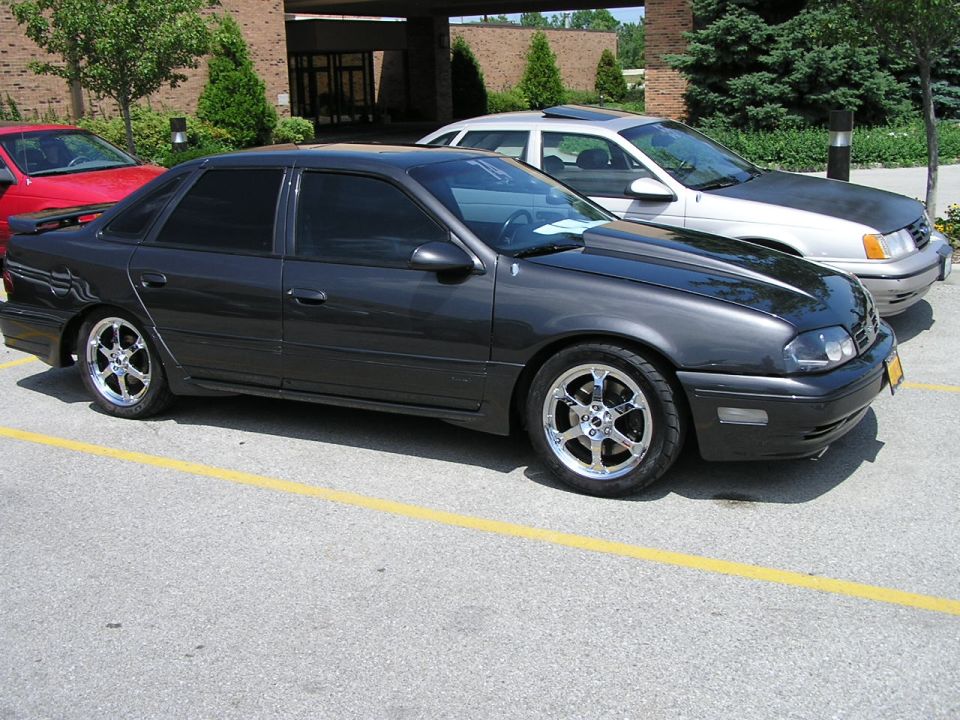 Dark gray sedan with aftermarket wheels and hood scoop, 3q front view