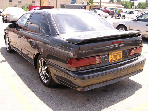 1993 Ford Taurus - A dark gray 1993 Ford Taurus SHO sedan is parked outdoors, showing its rear end and custom wheels.