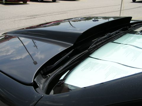 1993 Ford Taurus - A close-up view of a black car's hood scoop, with papers visible on the dashboard and other vehicles in the background.