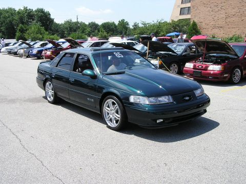 1993 Ford Taurus - A dark green 1993 Ford Taurus is parked at a car show with other vehicles in the background.