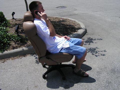 1993 Ford Taurus - Man sits in an office chair on pavement, talking on his phone.