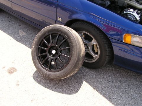1993 Ford Taurus - A blue 1993 Ford Taurus is parked on asphalt with a spare black wheel and tire placed in front of its front wheel.